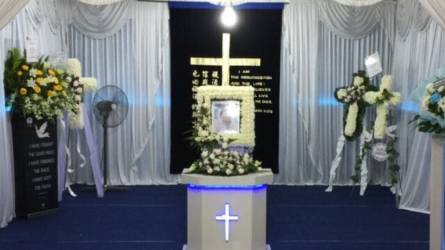 Christian funeral service setup at Singapore Funeral with a cross backdrop and floral wreaths.